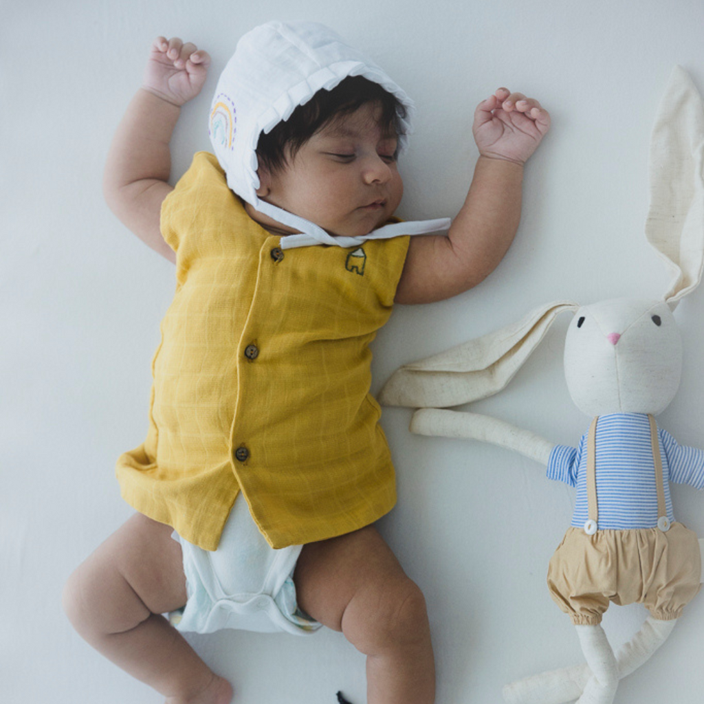Organic cotton muslin newborn vest in chic pastel shades with hand-embroidered details including Saturn planet and crown. Eco-friendly wooden button closure. Perfect for stylish and breathable all-season wear for your little one.